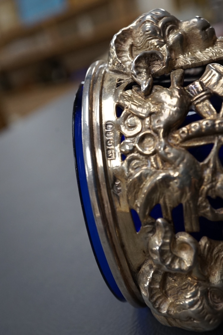 A late Victorian continental pierced silver posy vase, with blue glass liner, decorated with cupids, ram's heads and birds, on tripod supports with hoof feet, import marks for William Moering, London, 1898, height 15.2cm